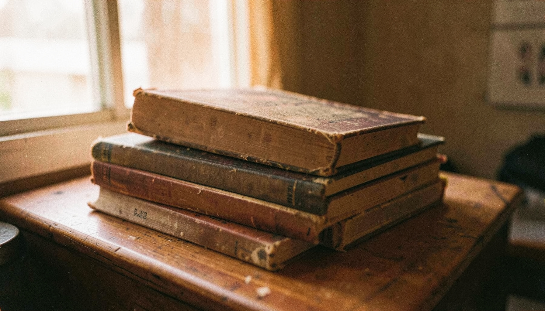 A warm-toned analog photograph of well-worn anthropology books stacked on a wooden desk, with visible grain and soft natural light from a window.