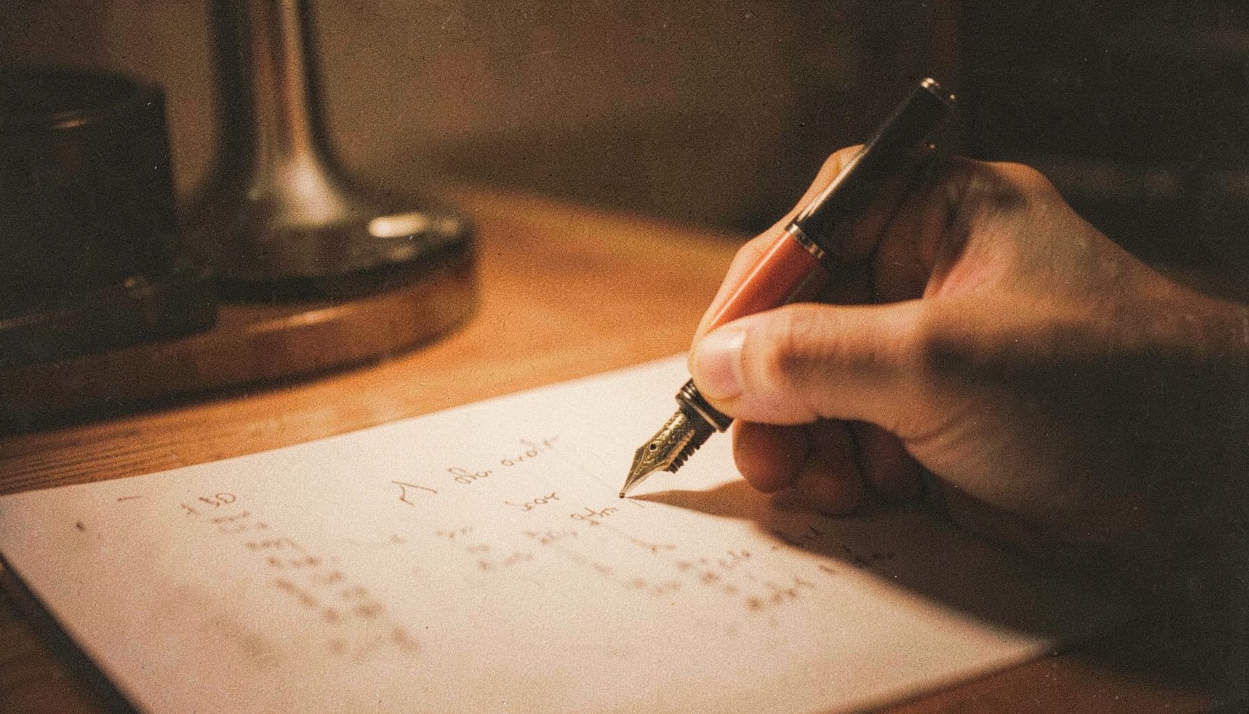 A grainy analog photo of a hand writing a note on paper with a fountain pen, warm desk-lamp glow, deep browns and creams.